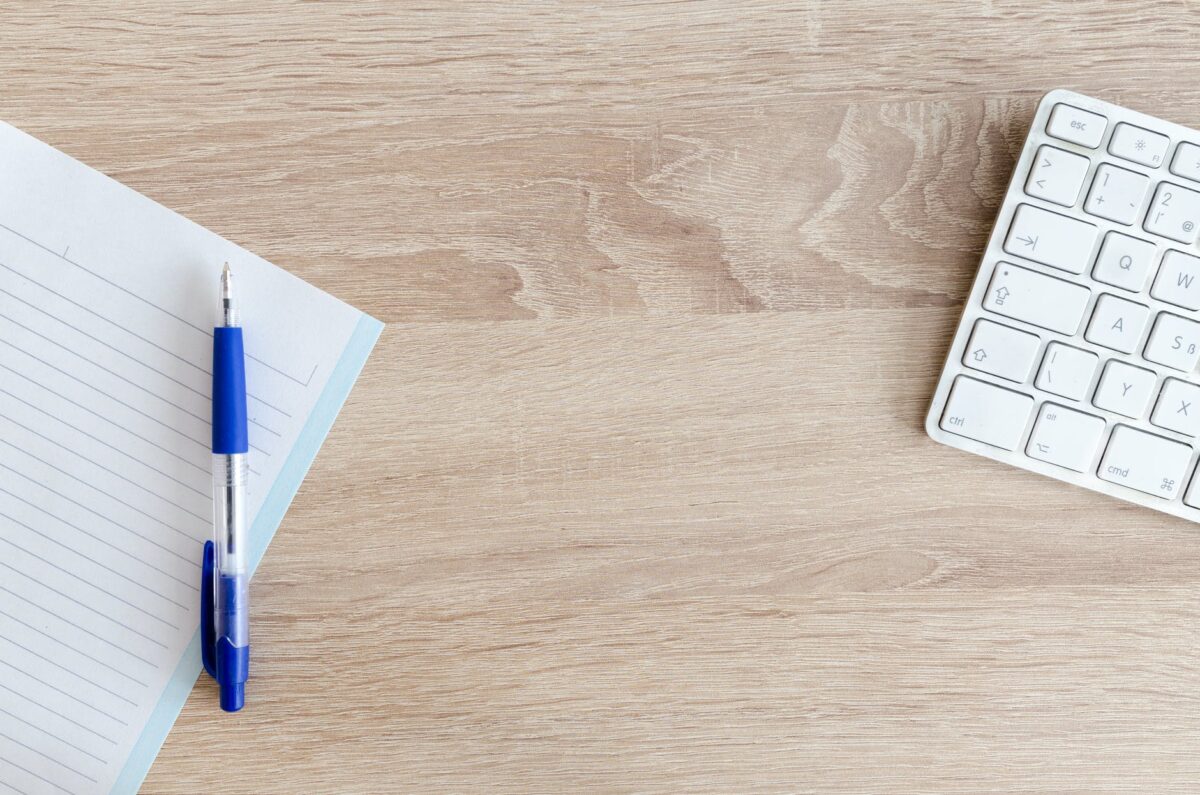 blue retractable pen on top of notebook near magic keyboard