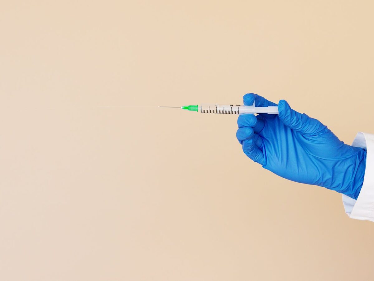 crop nurse with syringe on beige background